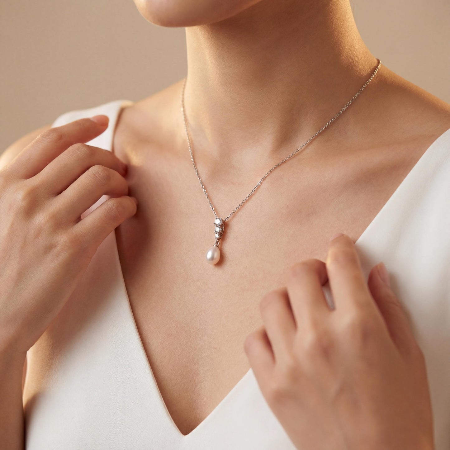 Person wearing a delicate necklace with a pearl pendant, hands adjusting it.