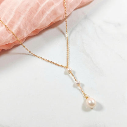Gold necklace with pearls on a light pink fabric background