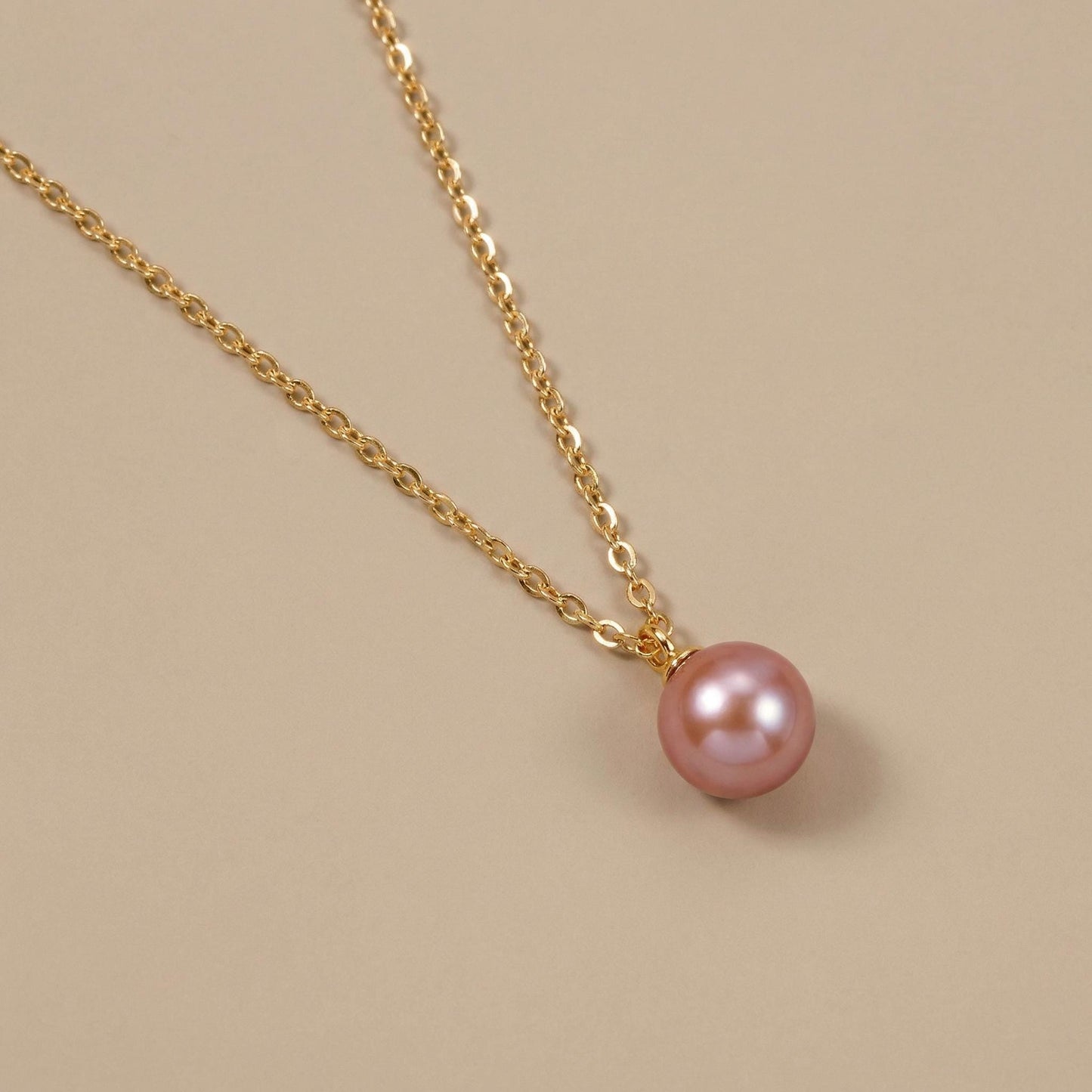 Gold necklace with a pink pearl pendant on a beige background
