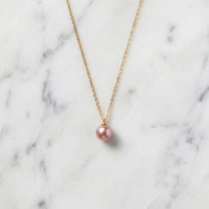 Gold necklace with a pink pearl pendant on a marble background