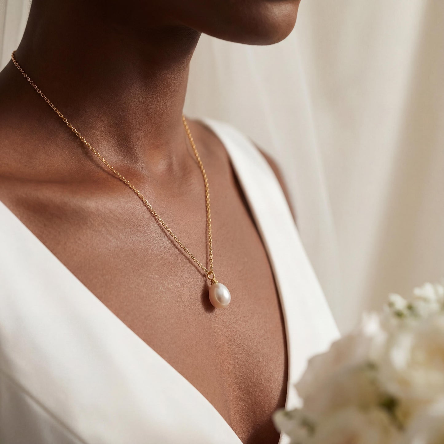 Close-up of a person wearing a gold necklace with a pearl pendant, holding flowers.