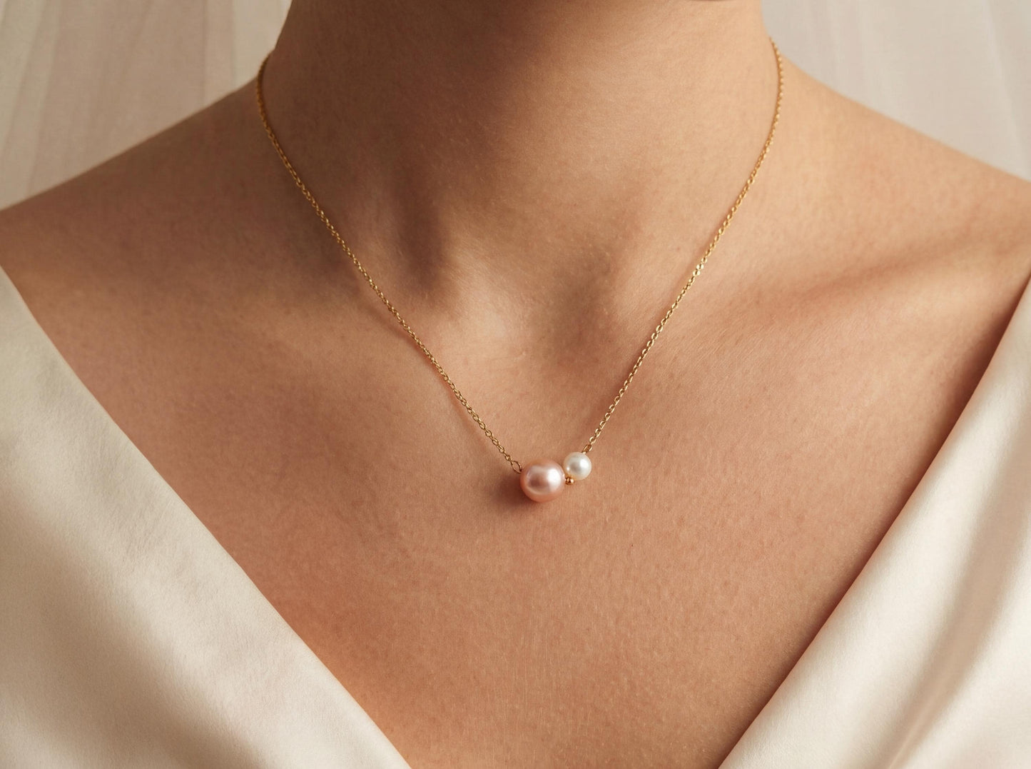 Gold necklace with a pearl pendant on a person wearing a white garment.