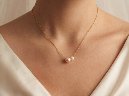 Gold necklace with a pearl pendant on a person wearing a white garment.
