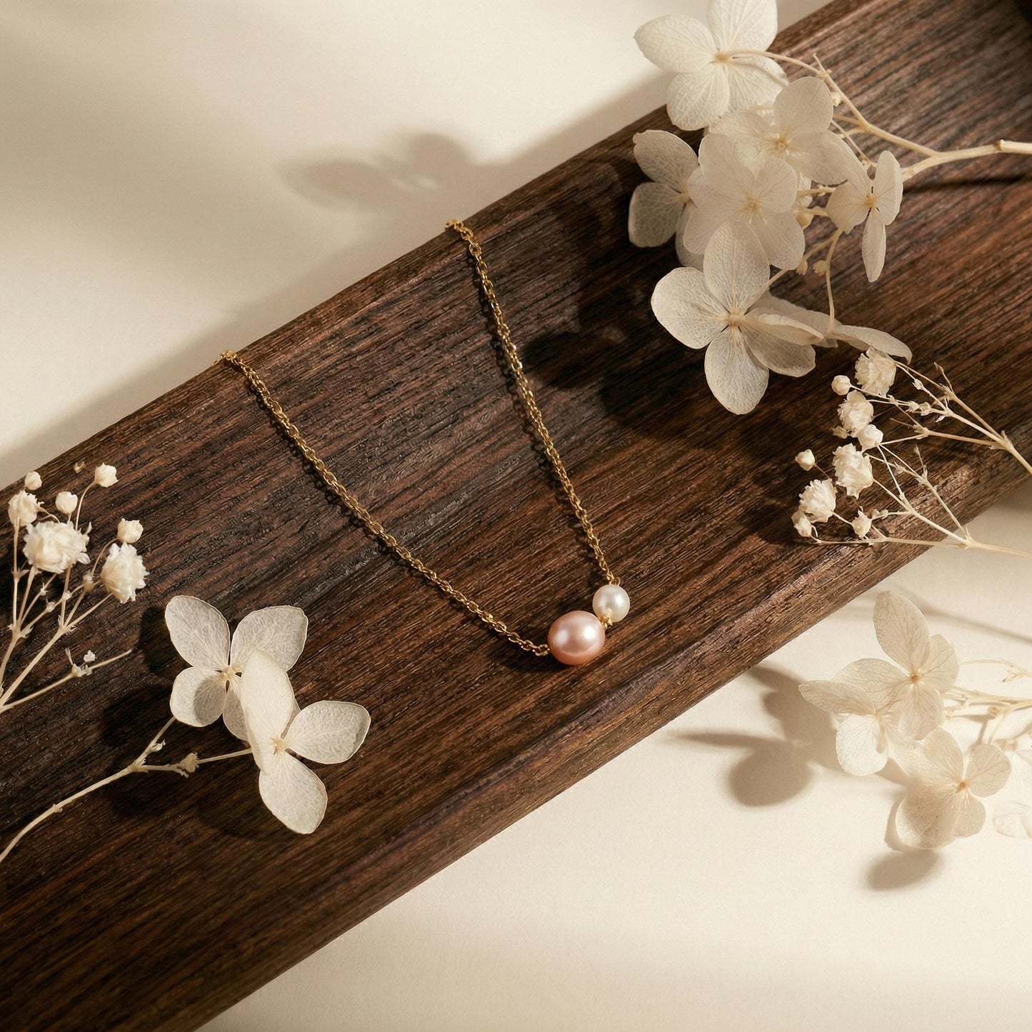 Necklace with a pink pearl pendant on a wooden surface with white flowers.